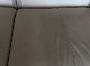 Close-up of white leather sofa seat prior to cleaning, showing surface dullness and soiling from regular use